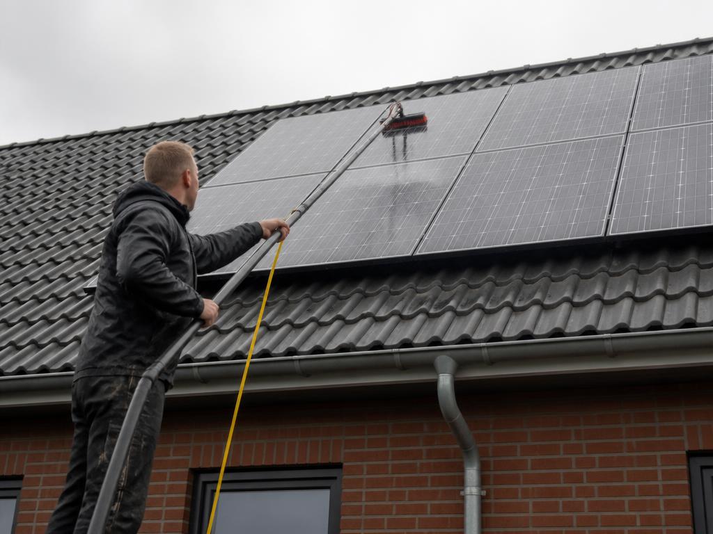 Solcellepaneler på tag der bliver vasket med teleskopbørste